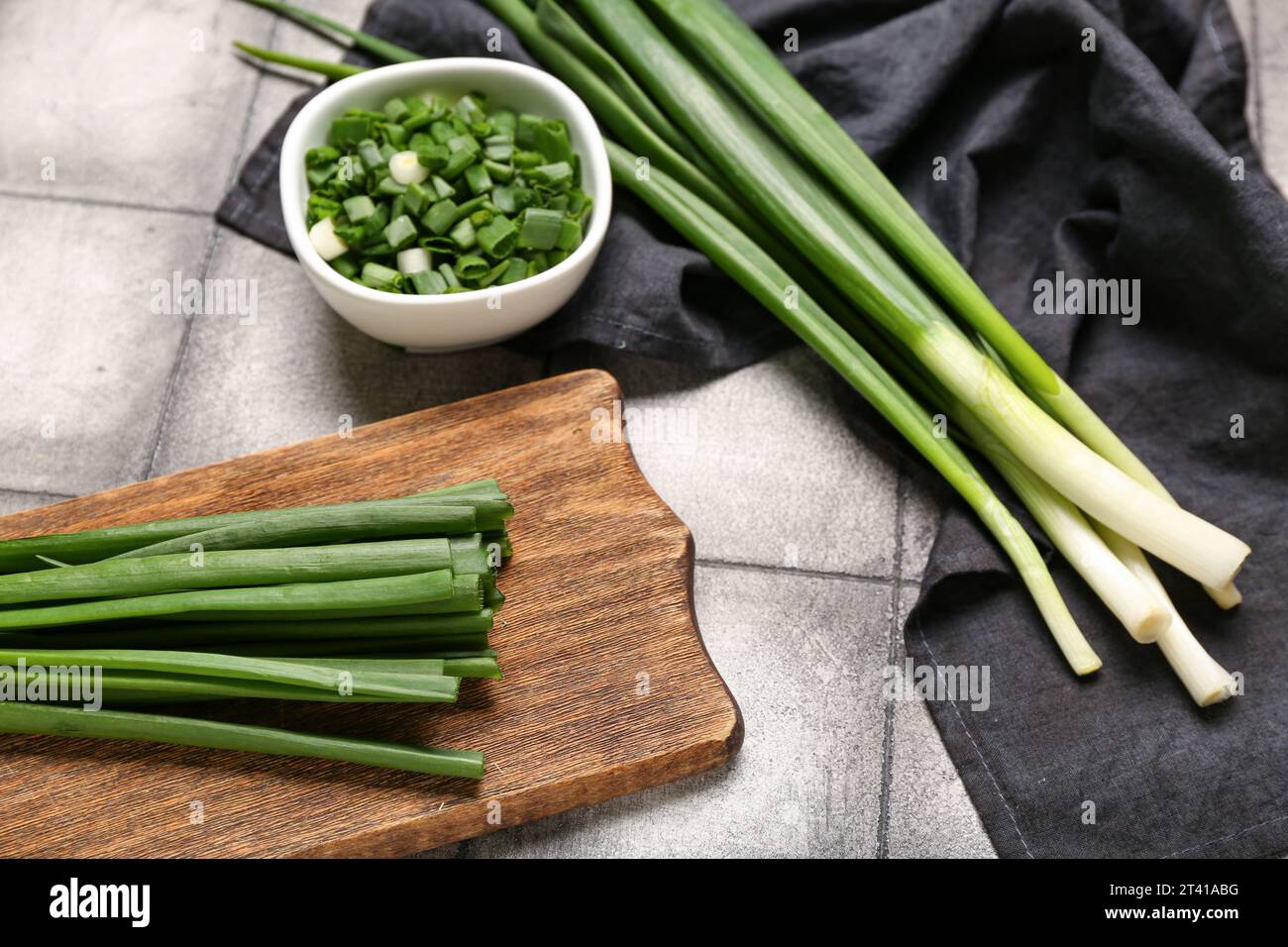 Wooden board and bowl with fresh green onion on dark tile background ...