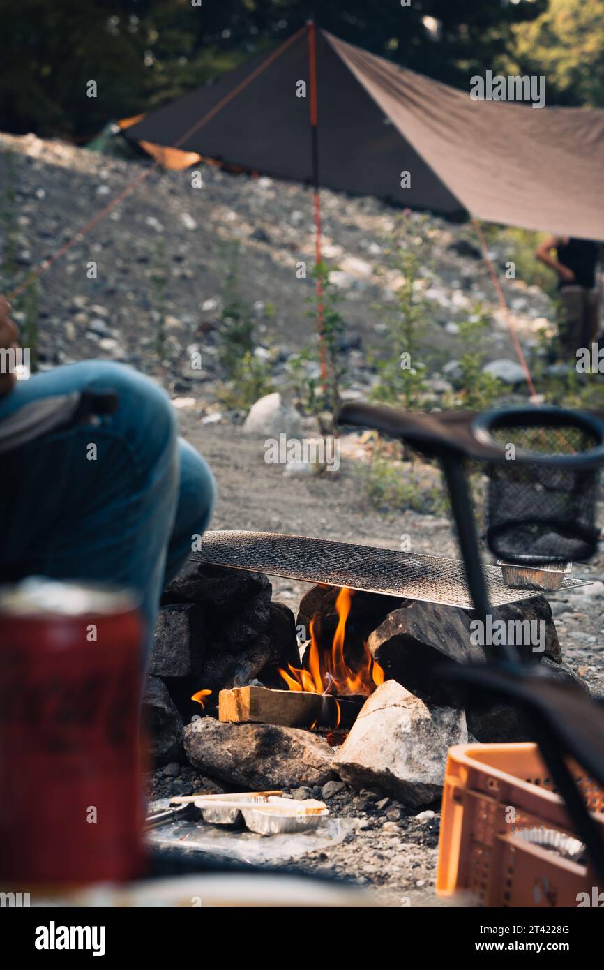 A group of people gathered around a campfire, with a tent set up nearby in Okutama, Japan Stock Photo