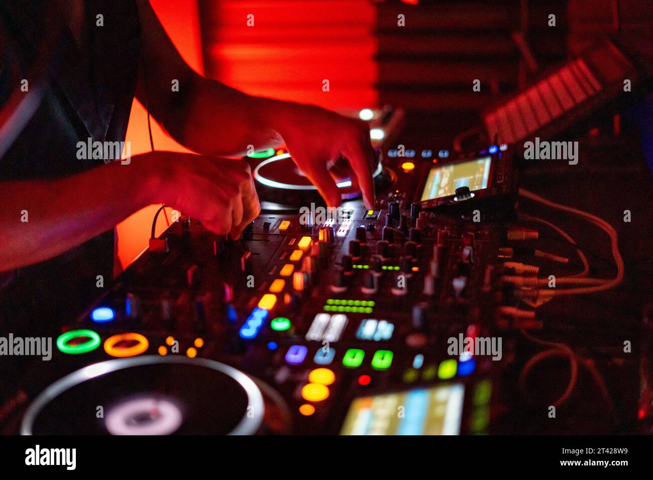 A DJ working on a professional controller in a dimly lit room, with illuminated buttons Stock Photo