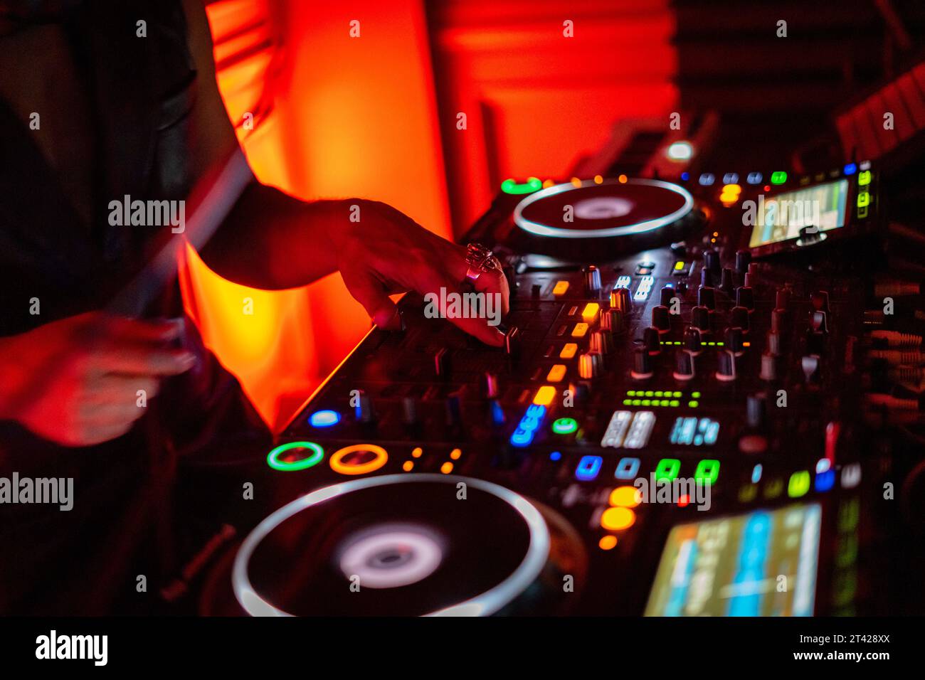 A DJ working on a professional controller in a dimly lit room, with illuminated buttons Stock Photo