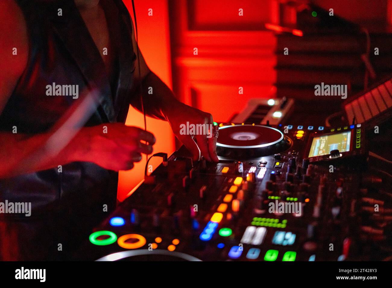 A DJ working on a professional controller in a dimly lit room, with illuminated buttons Stock Photo