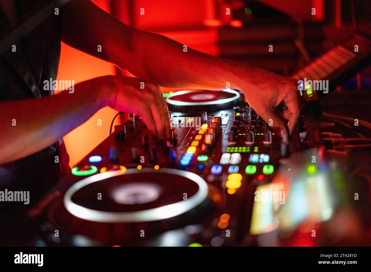 A DJ working on a professional controller in a dimly lit room, with illuminated buttons Stock Photo