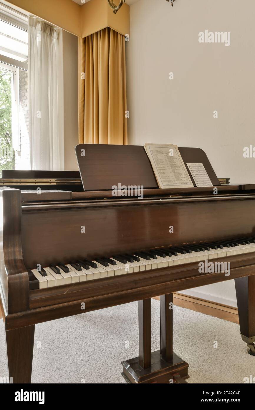 a living room with a piano on the floor and windows in the photo is taken from inside, while it's still showing Stock Photo