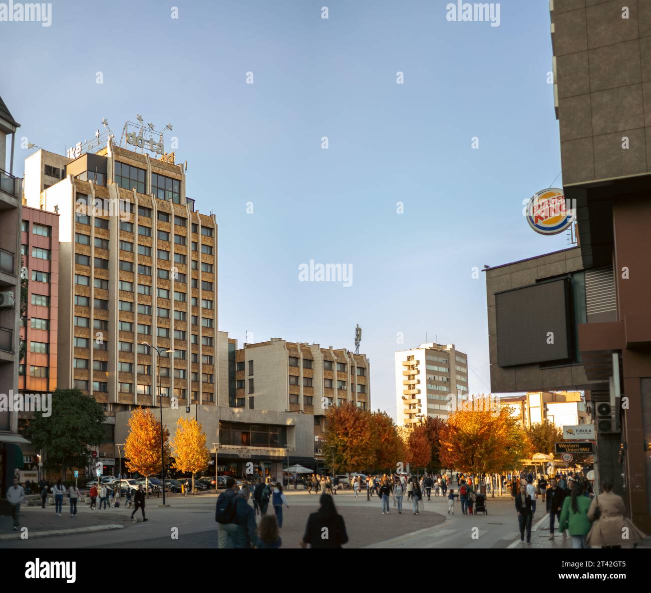 A vibrant intersection of city buildings and pedestrians in a sun ...