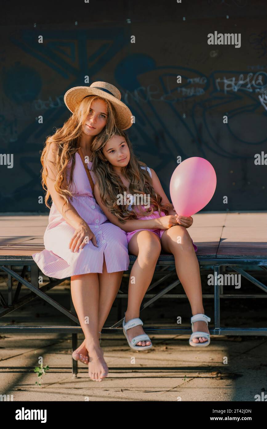 Portrait of mother and daughter in pink dresses with flowing long hair ...