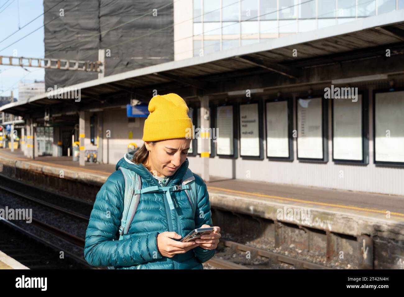 A young woman stands in a busy train station, engrossed in her cell phone Stock Photo