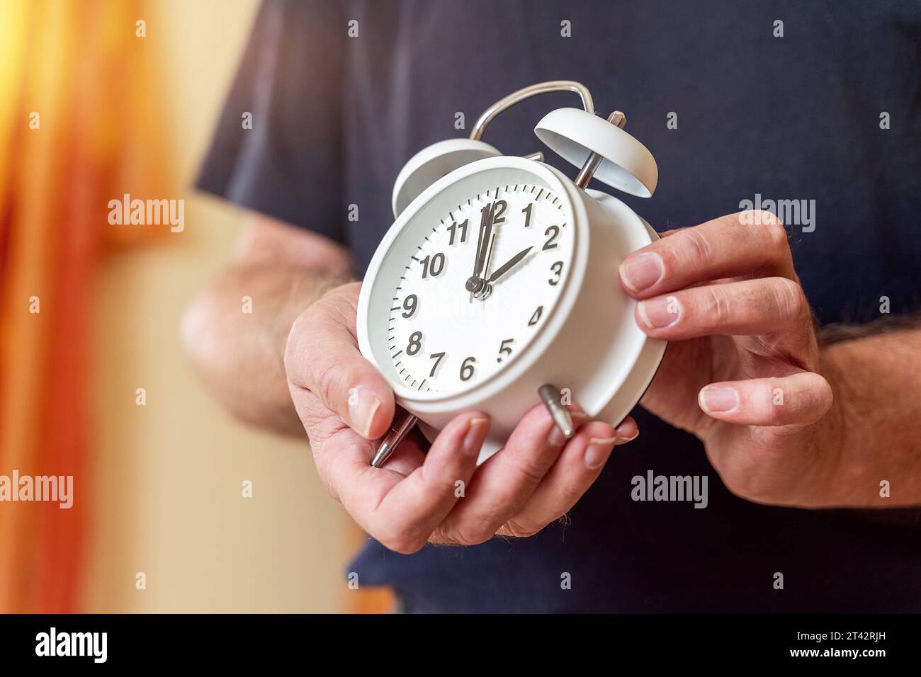 Augsburg, Bavaria, Germany. 27th Oct, 2023. Old man sets the clock on an alarm clock from