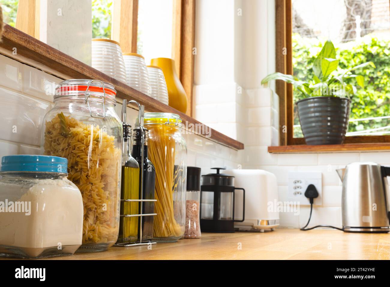 Food storage jars on windowsill and worktop, with plant and appliances in kitchen Stock Photo