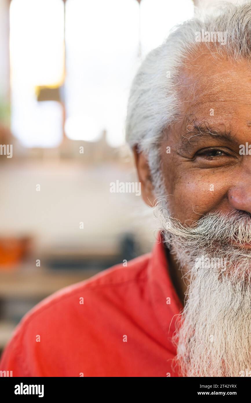 Half face of happy biracial senior man with long beard, smiling in pottery studio Stock Photo