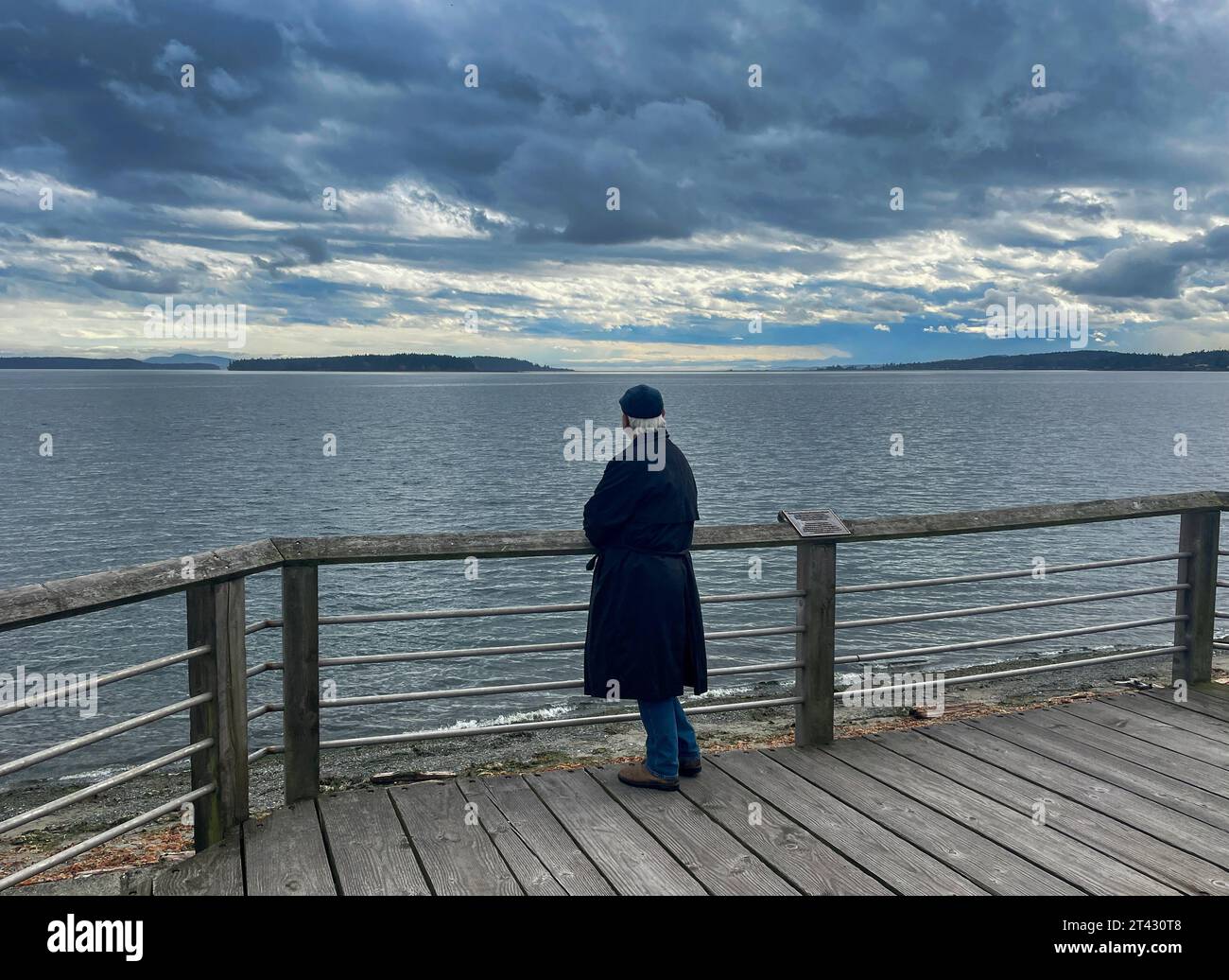 Rear view of a man standing on a jetty looking out to sea on an overcast day, Sidney, British Columbia, Canada Stock Photo