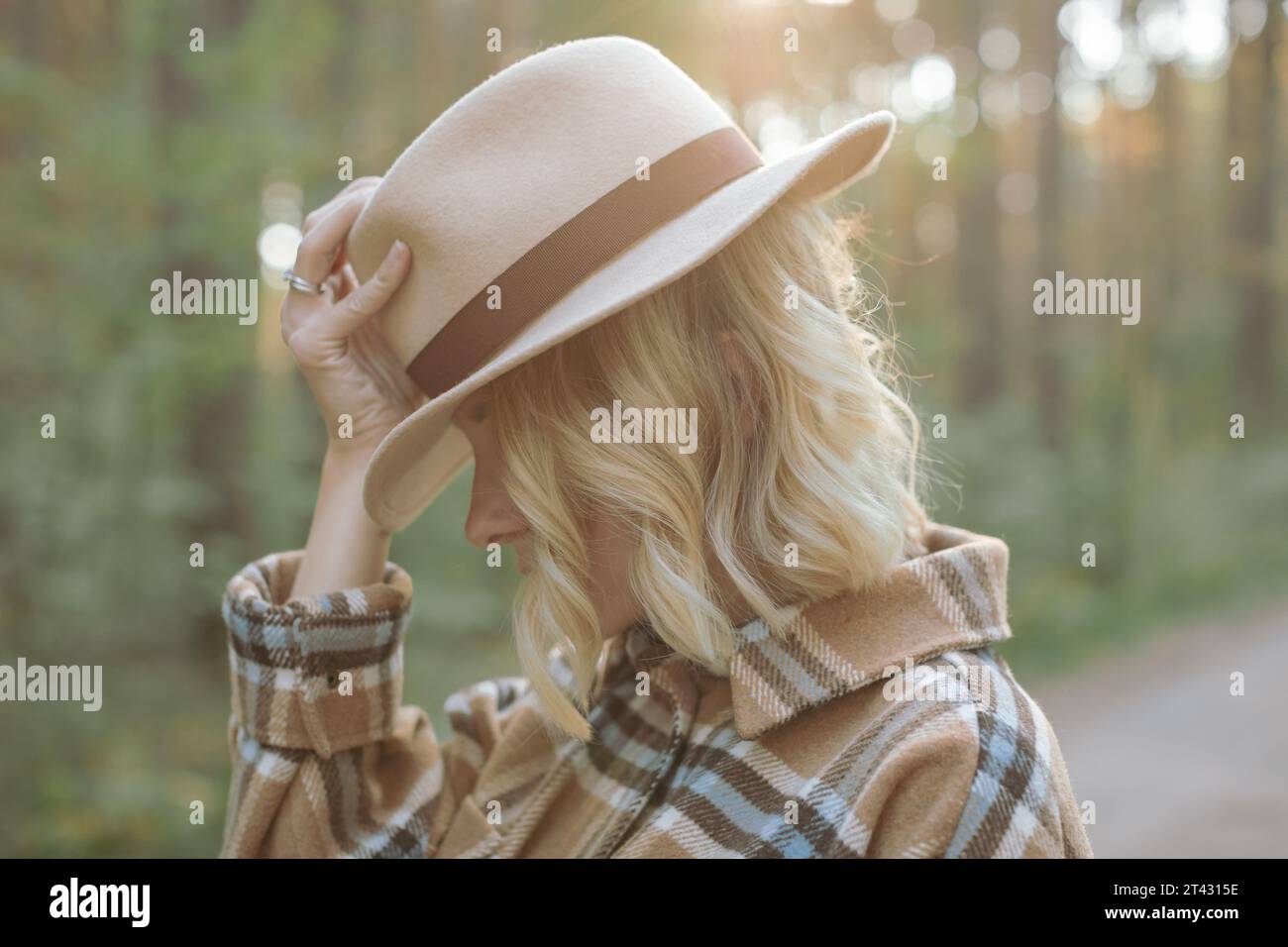 Portrait of a stylish young woman standing in a forest with her hand on her hat, Belarus Stock Photo
