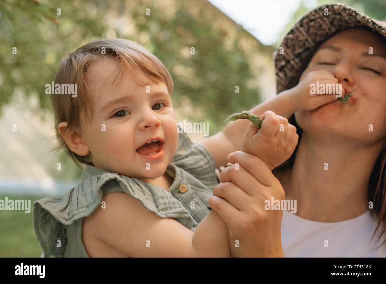 Mother holding her daughter who is putting a leaf in her mouth, Belarus Stock Photo