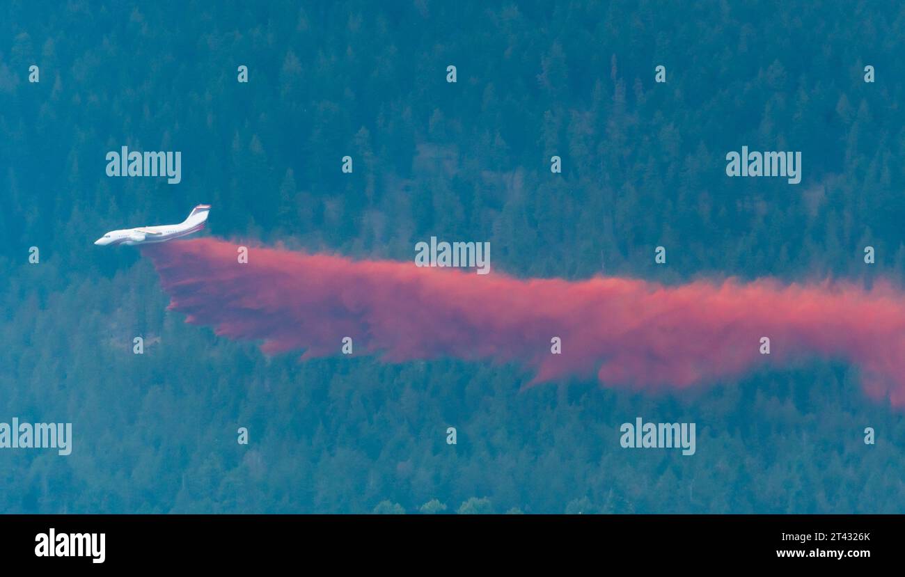 Firefighting aircraft in flight dropping Red fire Retardant over a forest in summer, Kelowna, Okanagan Valley, British Columbia, Canada Stock Photo