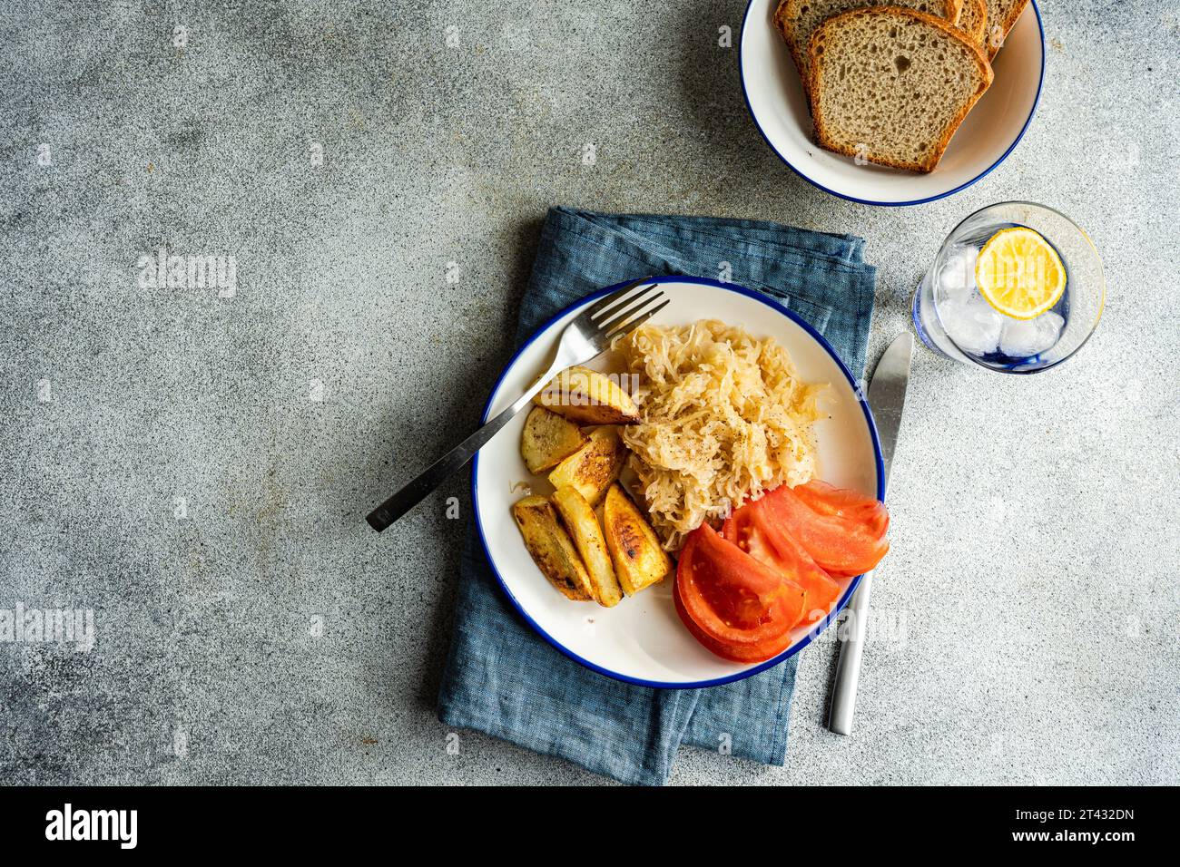 Overhead view of a fermented cabbage salad with baked potato, tomato, bread and a glass of lemon ice water Stock Photo