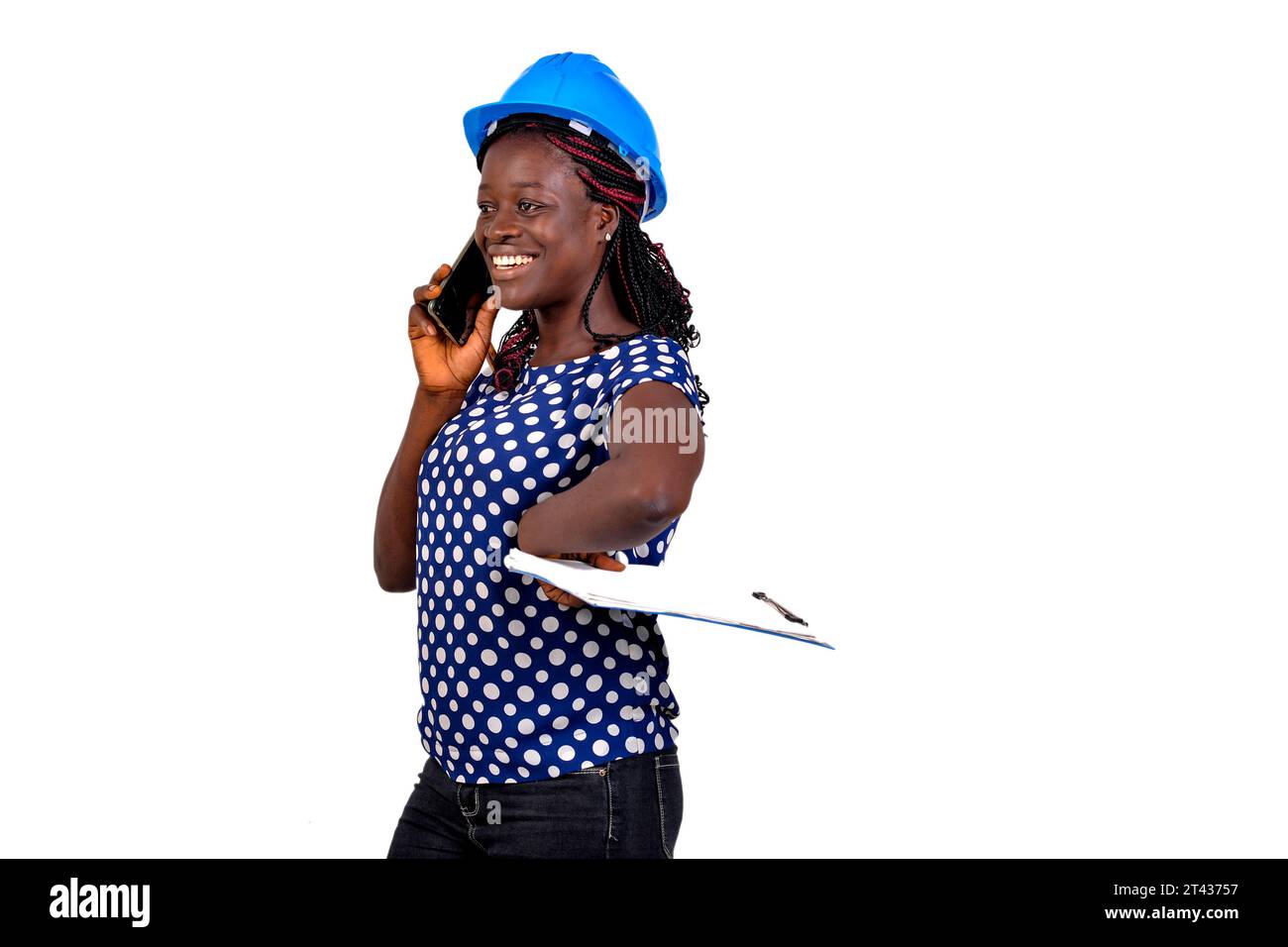 young female construction engineer holding clipboard and talking on mobile phone while smiling. Stock Photo