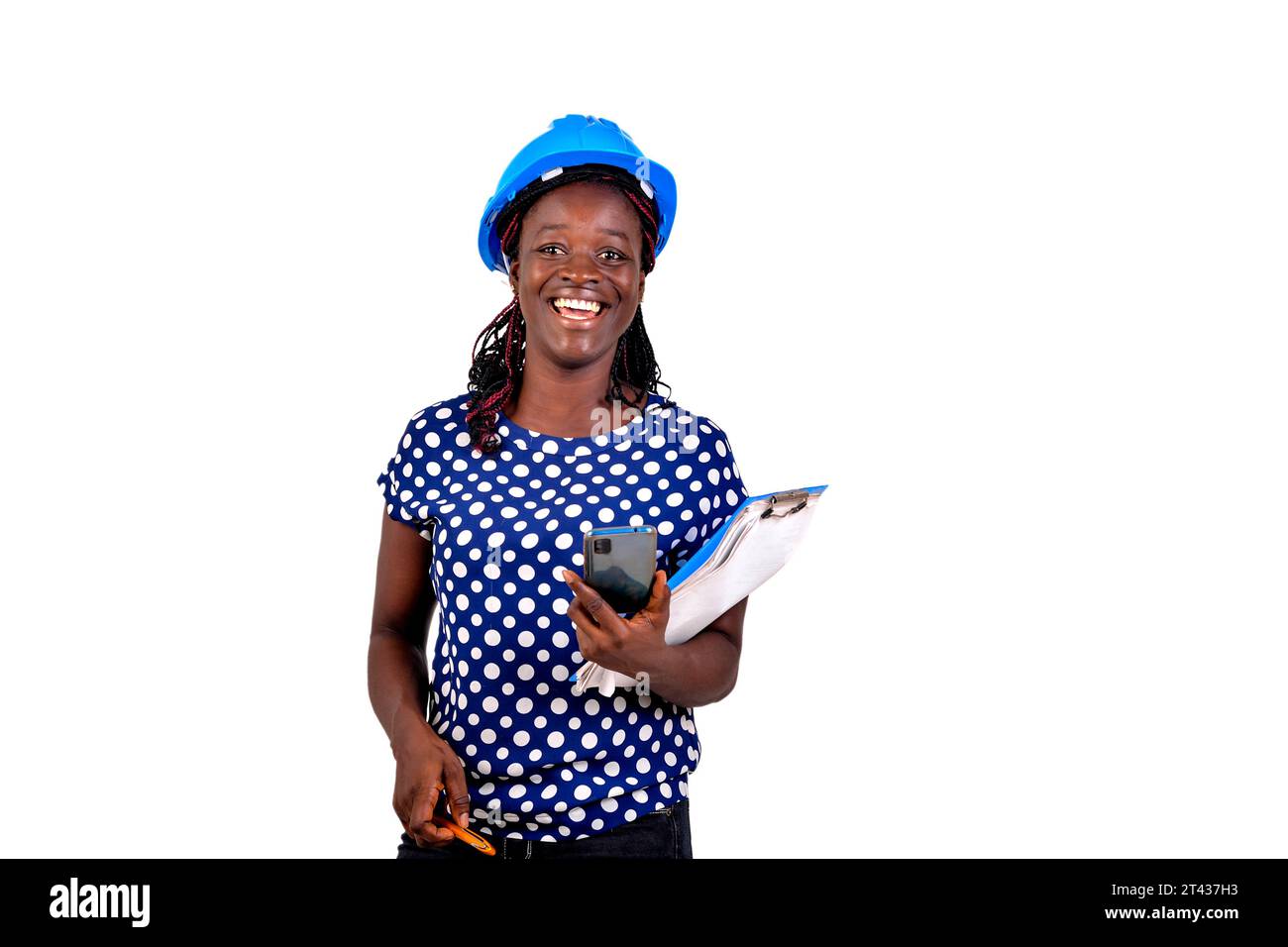 beautiful young female construction engineer holding mobile phone and clipboard while smiling. Stock Photo