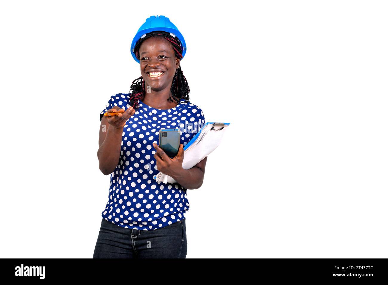 beautiful young female construction engineer holding mobile phone and clipboard while smiling. Stock Photo