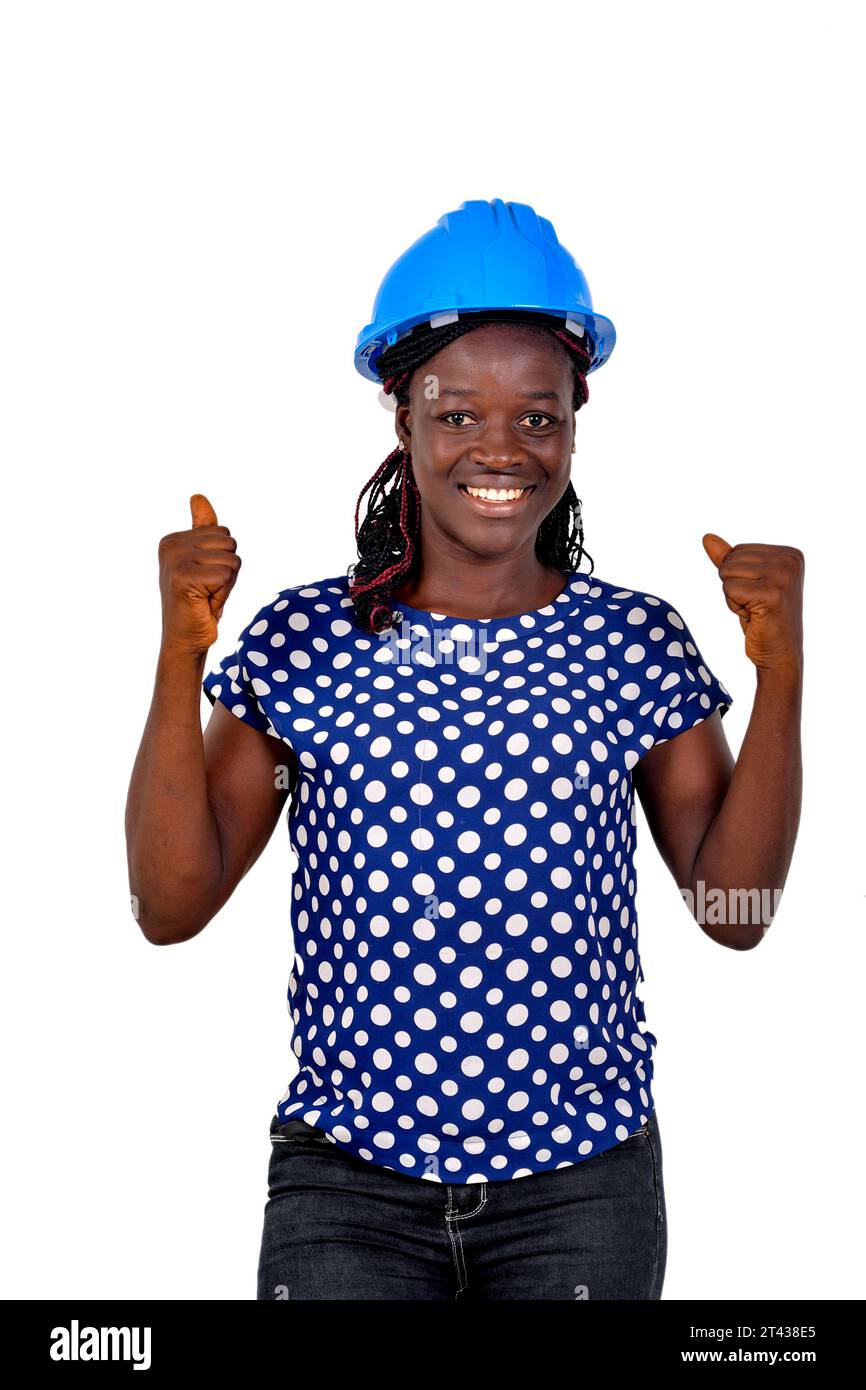 portrait of a beautiful happy young female engineer wearing a blue safety helmet and making a winning gesture while smiling. Stock Photo