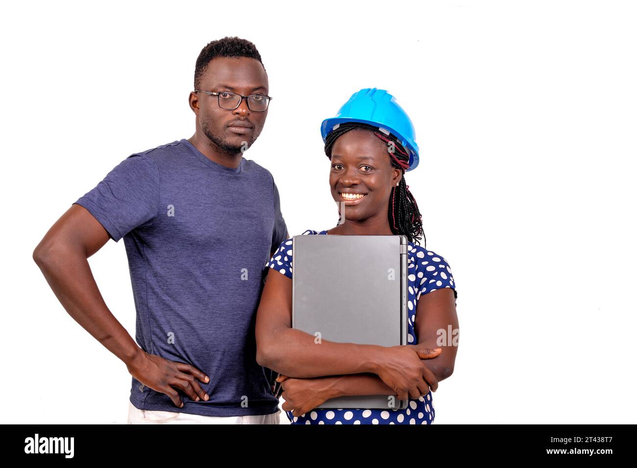 young man standing near female engineer wearing blue safety helmet with laptop while smiling. Stock Photo