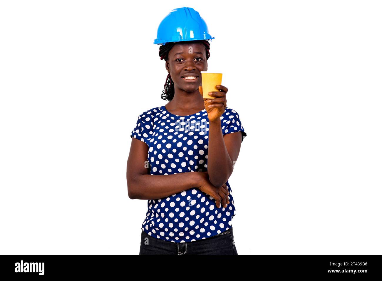portrait of a beautiful young female construction engineer wearing a blue hard hat holding a paper cup of coffee while smiling. Stock Photo