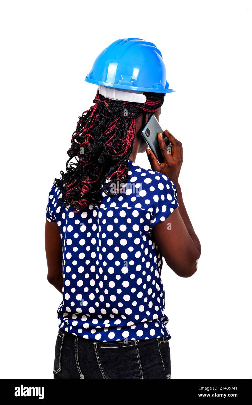 a beautiful female engineer with safety helmet standing on white background talking on the cell phone with her back to the camera. Stock Photo