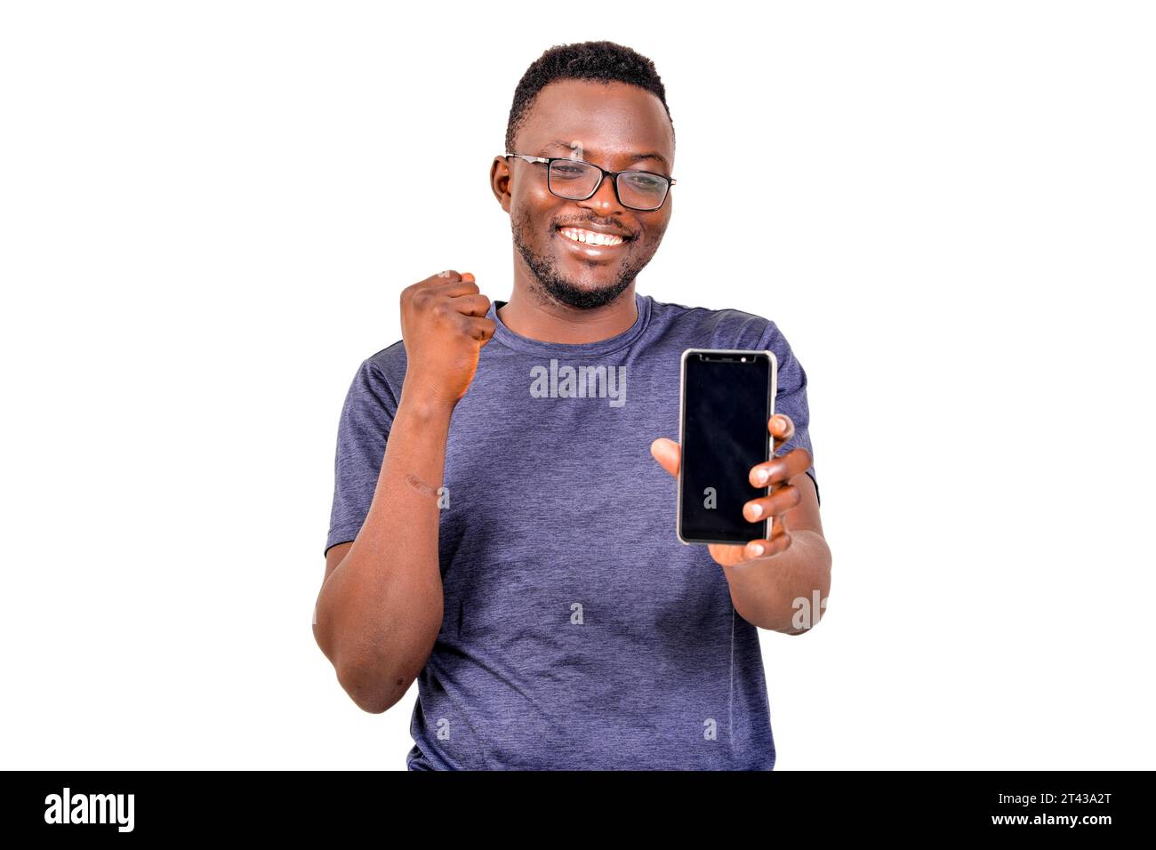 a handsome man in glasses standing on white background presenting cell phone and making victory gesture laughing. Stock Photo