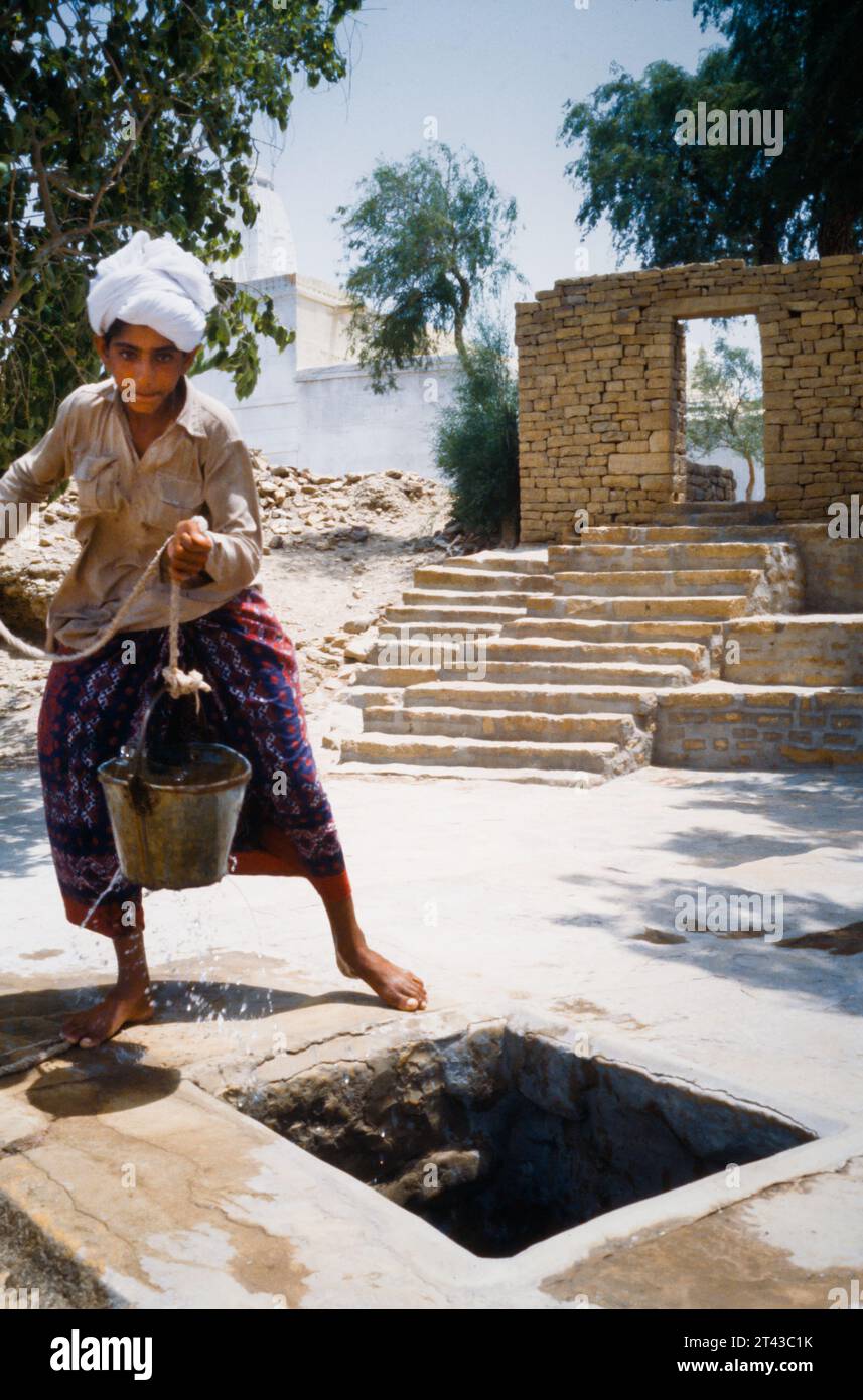 Archive, Historic Image Of A Rajhastani Boy In White Turban Holding A Leaky Metal Bucket On A Rope Fetching Water From A Well, Jaisalmer, India 1990 Stock Photo