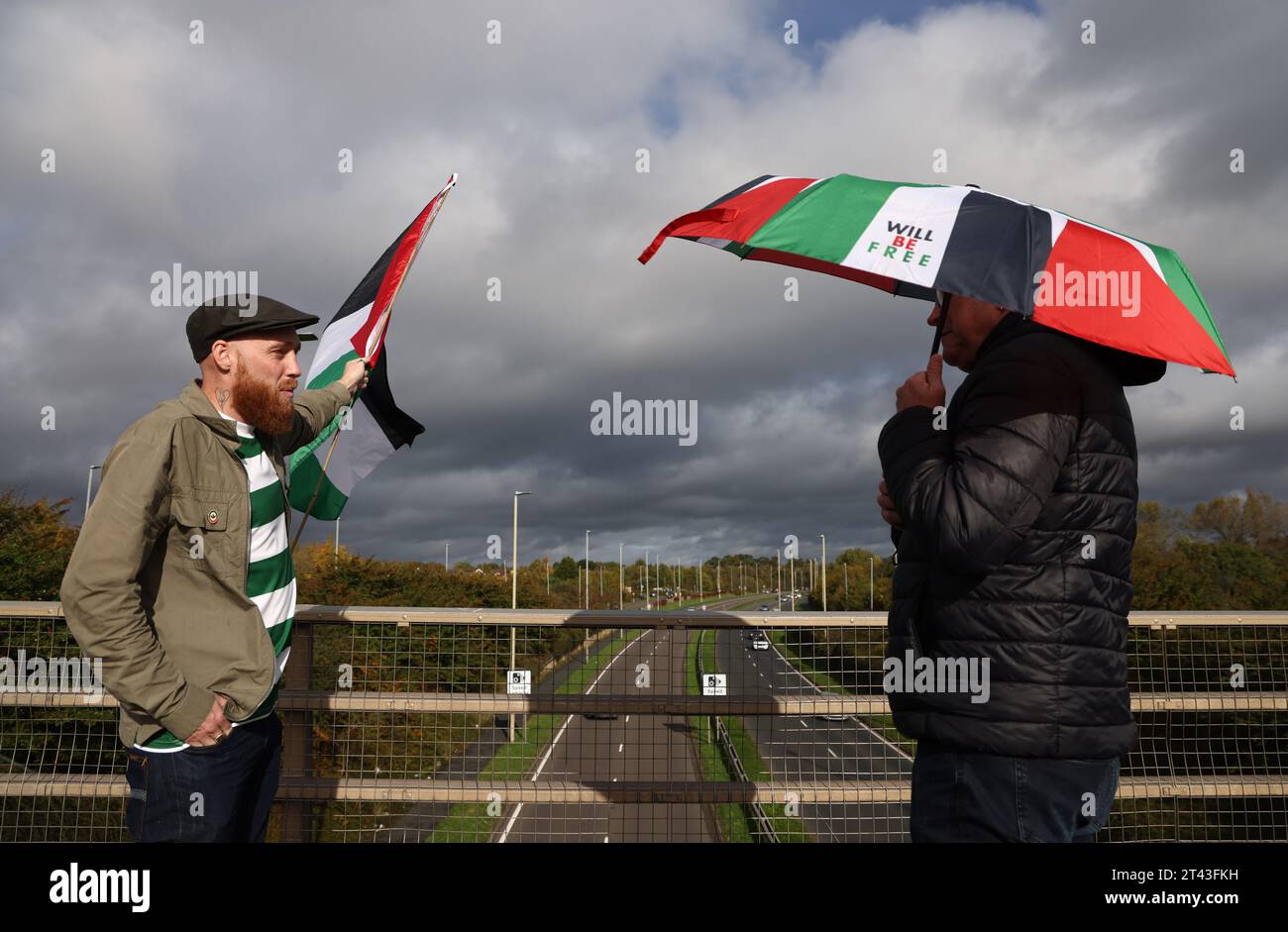 Leicester, Leicestershire, UK. 28th October 2023. A protester wearing a Celtic Football club shirt waves a flag during a pro-Palestinian demonstration and banner drop near to the base of UAV Tactical Systems. UAV Tactical Systems is an Israeli-French company manufacturing drones sold to the British army, Israel and international arms markets. Credit Darren Staples/Alamy Live News. Stock Photo