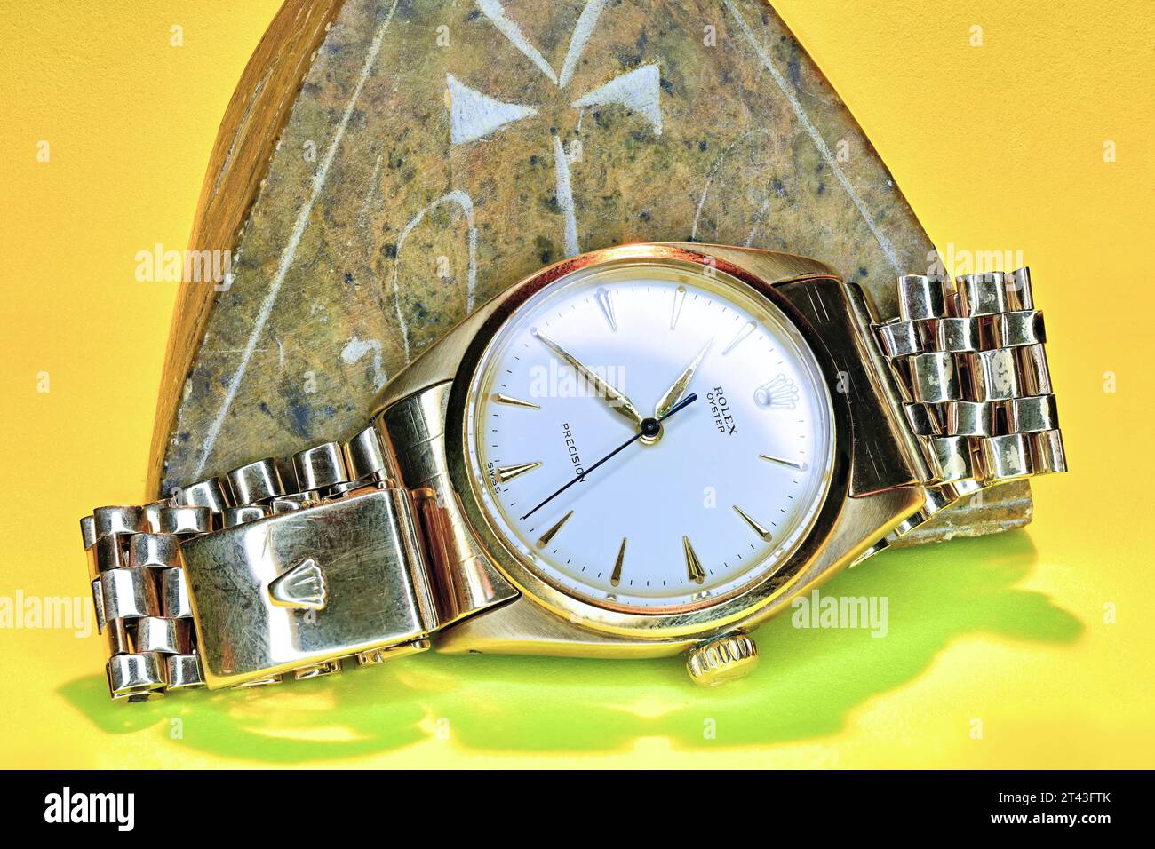 Gold Rolex Oyster wristwatch against a sand yellow background  and stone ankh pyramid Stock Photo