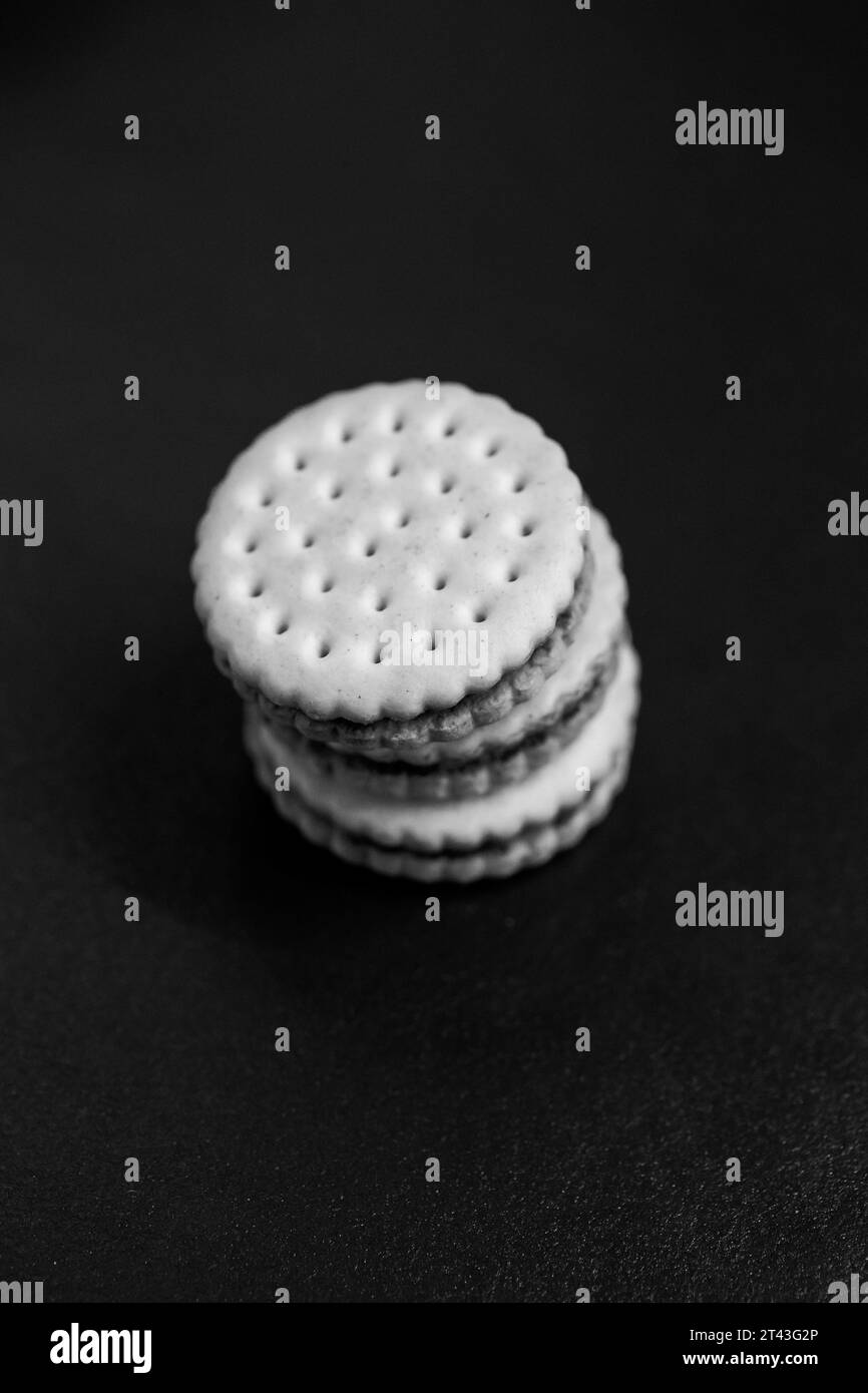 A black and white portrait of delicious round cookies with holes stacked on top of each other on a kitchen counter. The tasty snack has a biscuit on e Stock Photo