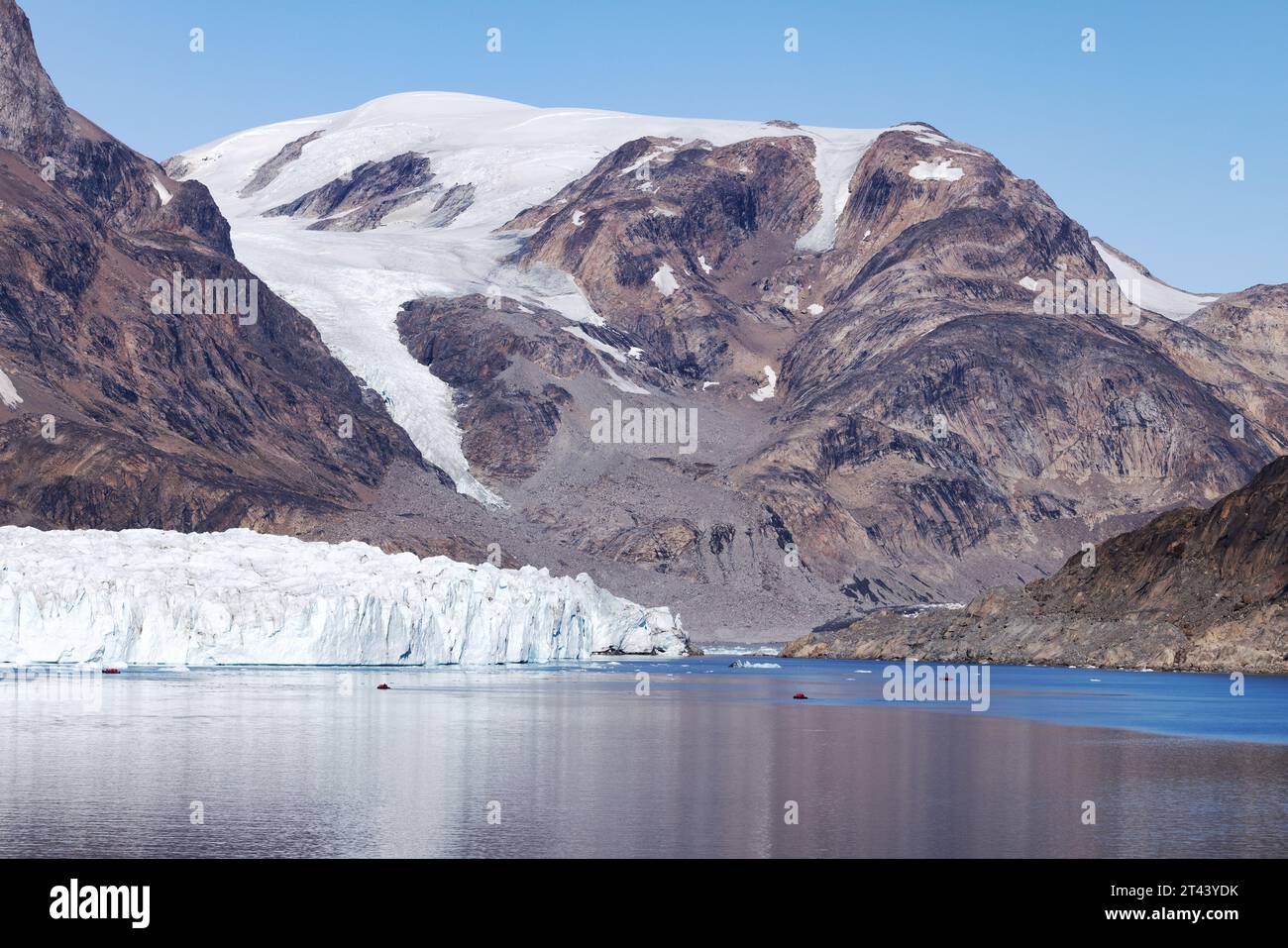 Greenland glacier; tiny tourist zodiacs seen visiting The Thrym Glacier at the end of Skjoldungen Fjord; Greenland Travel, Arctic travel. Stock Photo