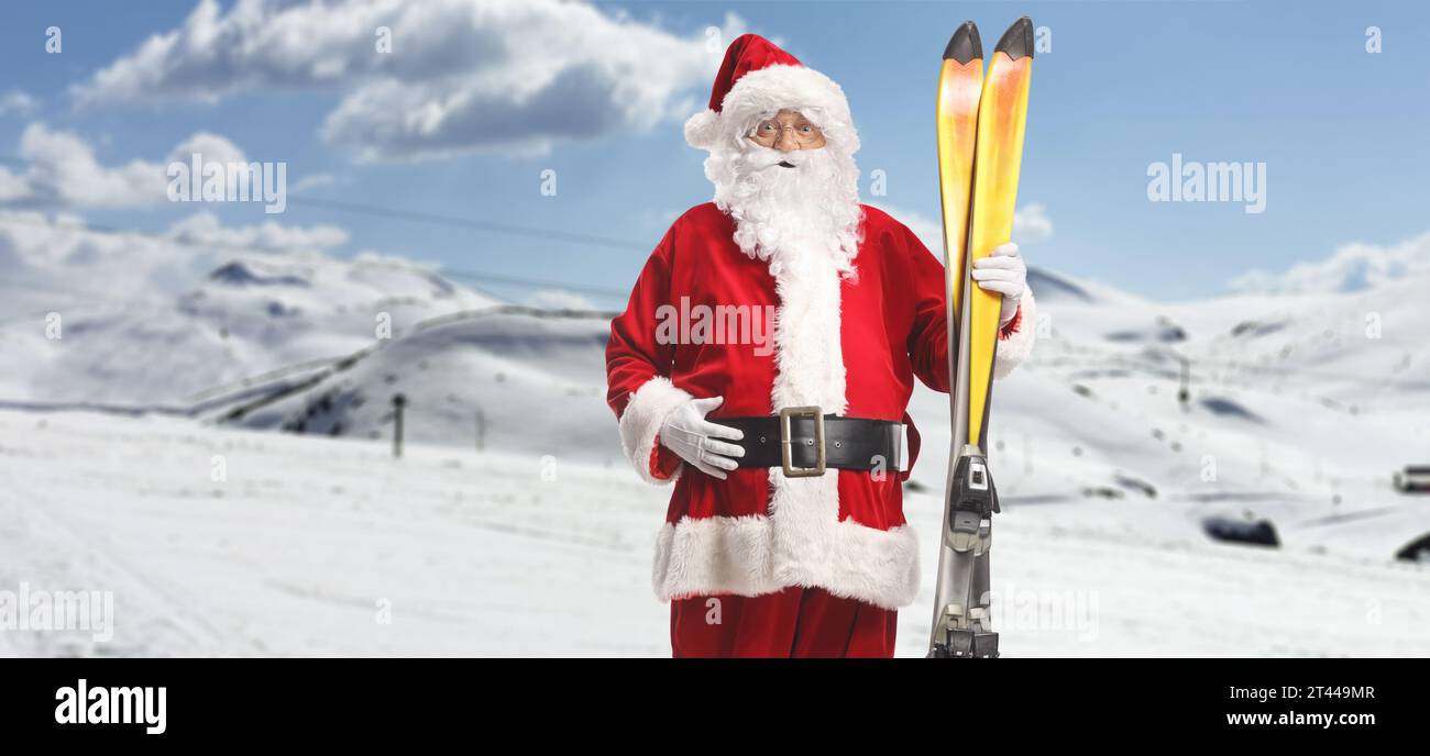 Santa Claus holding a pair of skis on a mountain hill Stock Photo