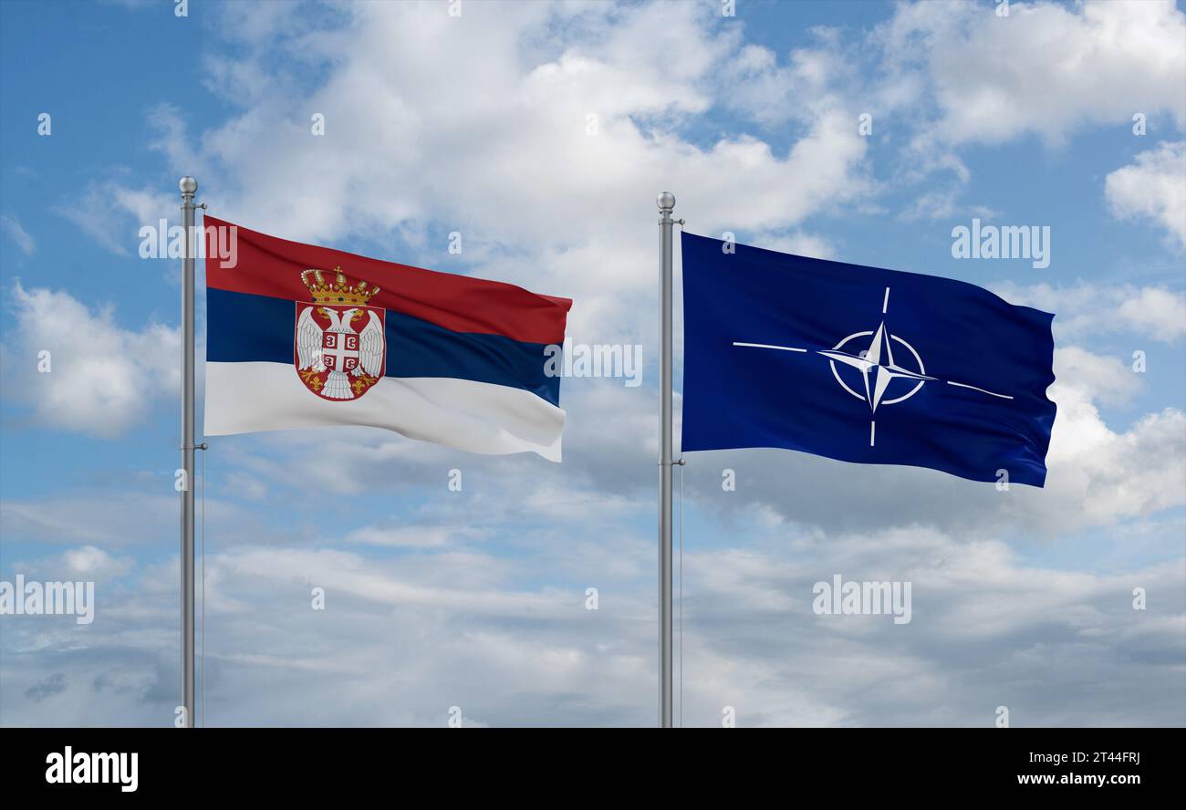NATO and Serbia flags waving together on blue cloudy sky, cooperation concept Stock Photo