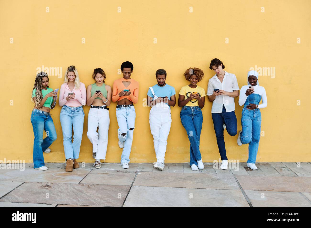 Multi-ethnic young people leaning on a wall using phone Stock Photo