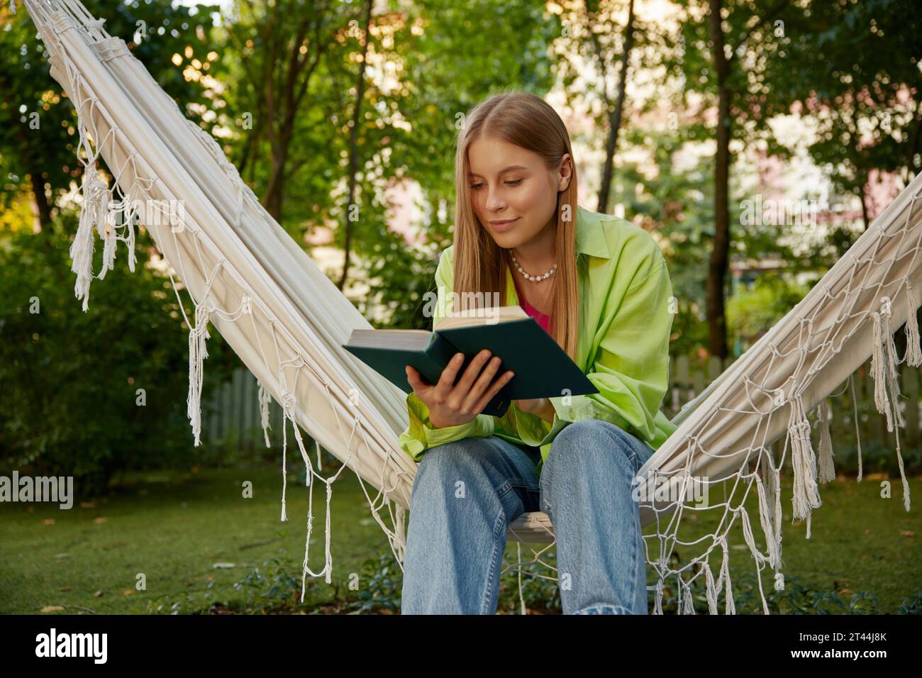 Cute woman relaxing in hanging hammock and reading the book Stock Photo ...