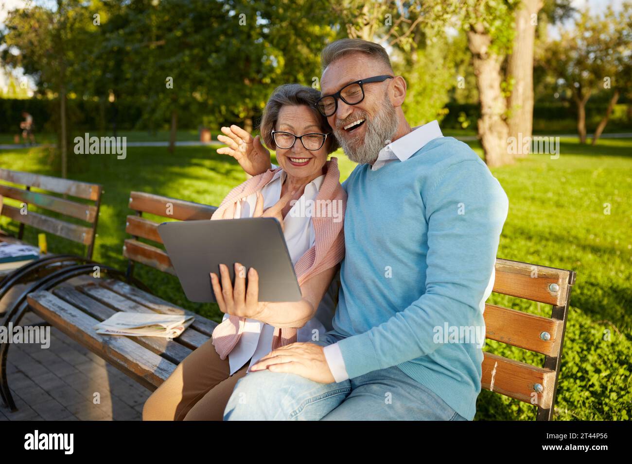 Smiling senior couple having videocall using digital tablet on park bench Stock Photo