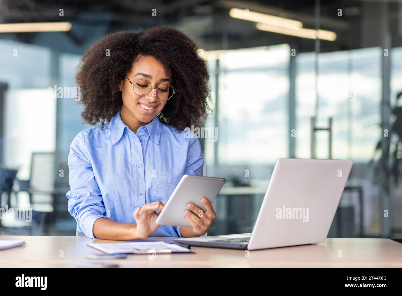 Young successful woman working with tablet computer inside office at workplace, smiling female programmer testing new app, writing code for software. Stock Photo