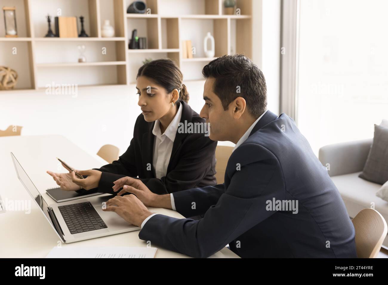 Two focused Indian professional colleagues discussing online application Stock Photo
