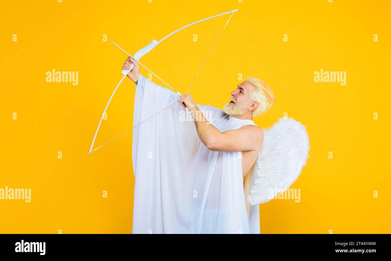 Valentines Day celebration. Arrow of love. Smiling blonde man in angel costume shooting love arrow. Valentine angel with white wings shoots love arrow Stock Photo