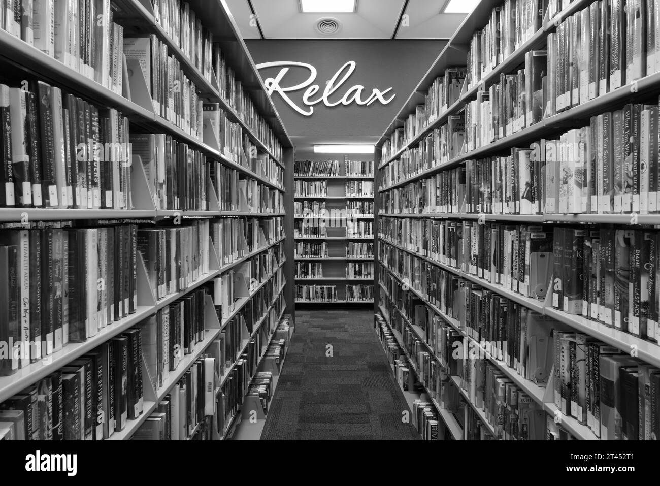 Books on shelves in a public library, with a 'Relax' sign on the wall Stock Photo
