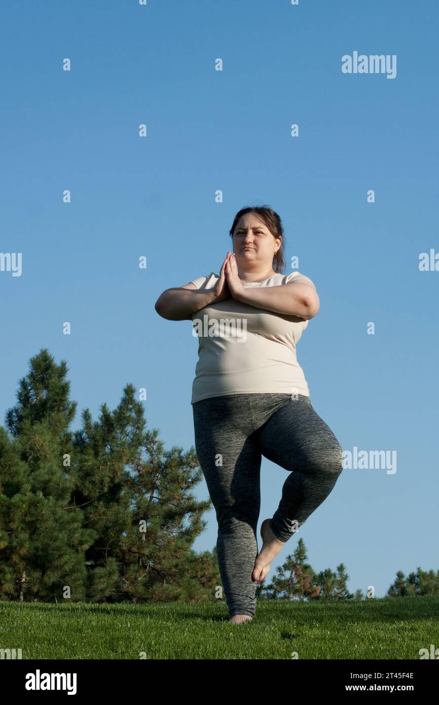 overweight middle-aged woman practices yoga outdoor barefoot, doing ...