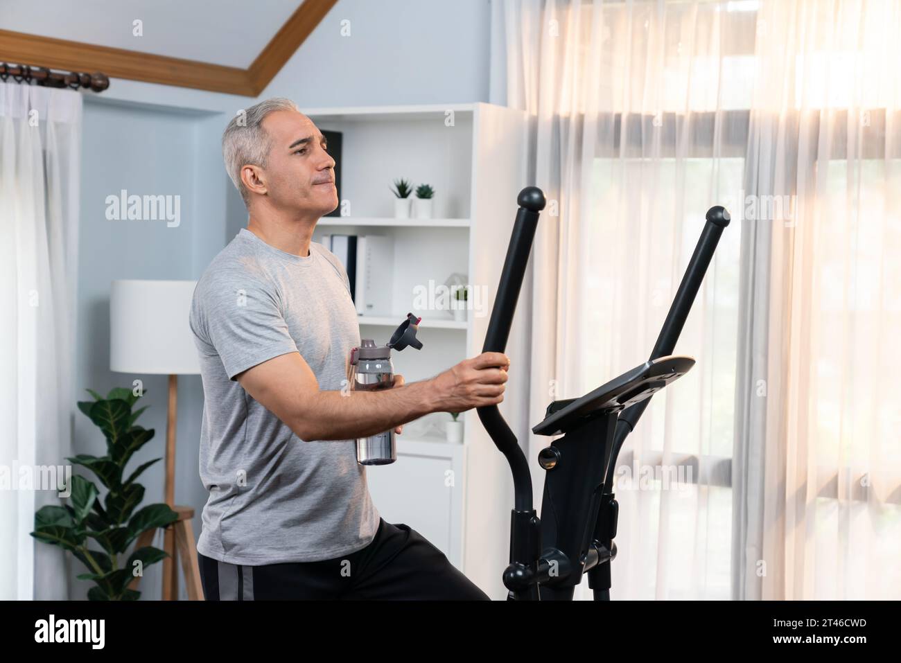Active senior man running on elliptical running machine and drinking ...