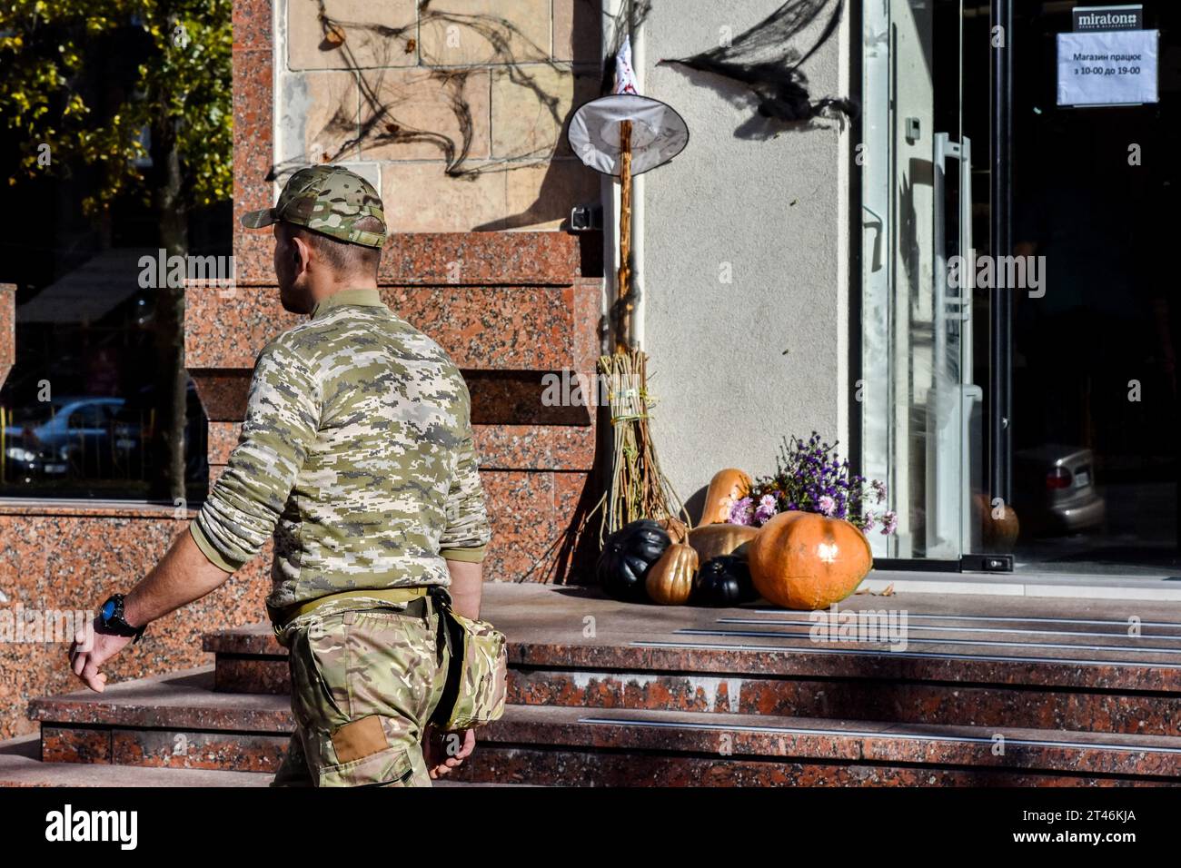 A Ukrainian army soldier is walking by the shop entrance with Halloween decorations in Zaporizhzhia. Halloween of Celtic origin came to Ukraine after the collapse of the Soviet Union. From that time the Ukrainians took over the tradition from other countries to dress in creepy costumes, to cut out the main attribute of this holiday - the pumpkin and to collect the candies among the neighbors. The modern Orthodox Church is still condemning this holiday, but every year in Ukraine are more and more young people who aren't against “going to the side of the evil” for one night. Stock Photo