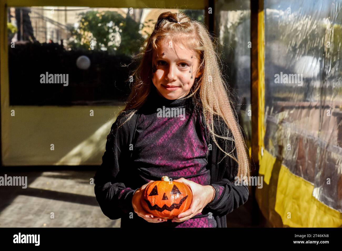 A little girl with a Halloween makeup posing with a natural pumpkin during the Halloween party. Halloween of Celtic origin came to Ukraine after the collapse of the Soviet Union. From that time the Ukrainians took over the tradition from other countries to dress in creepy costumes, to cut out the main attribute of this holiday - the pumpkin and to collect the candies among the neighbors. The modern Orthodox Church is still condemning this holiday, but every year in Ukraine are more and more young people who aren't against “going to the side of the evil” for one night. Stock Photo