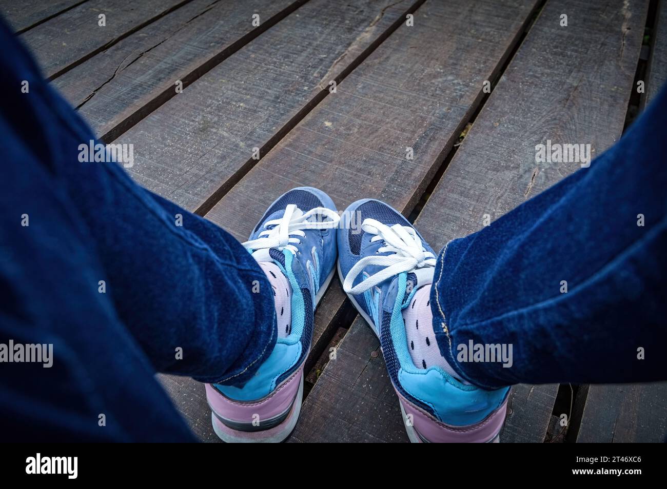 You can see legs wearing jeans and sport shoes from the perspective of the girl who is sitting on the wooden dock, Indonesia, 18 January 2015. Stock Photo