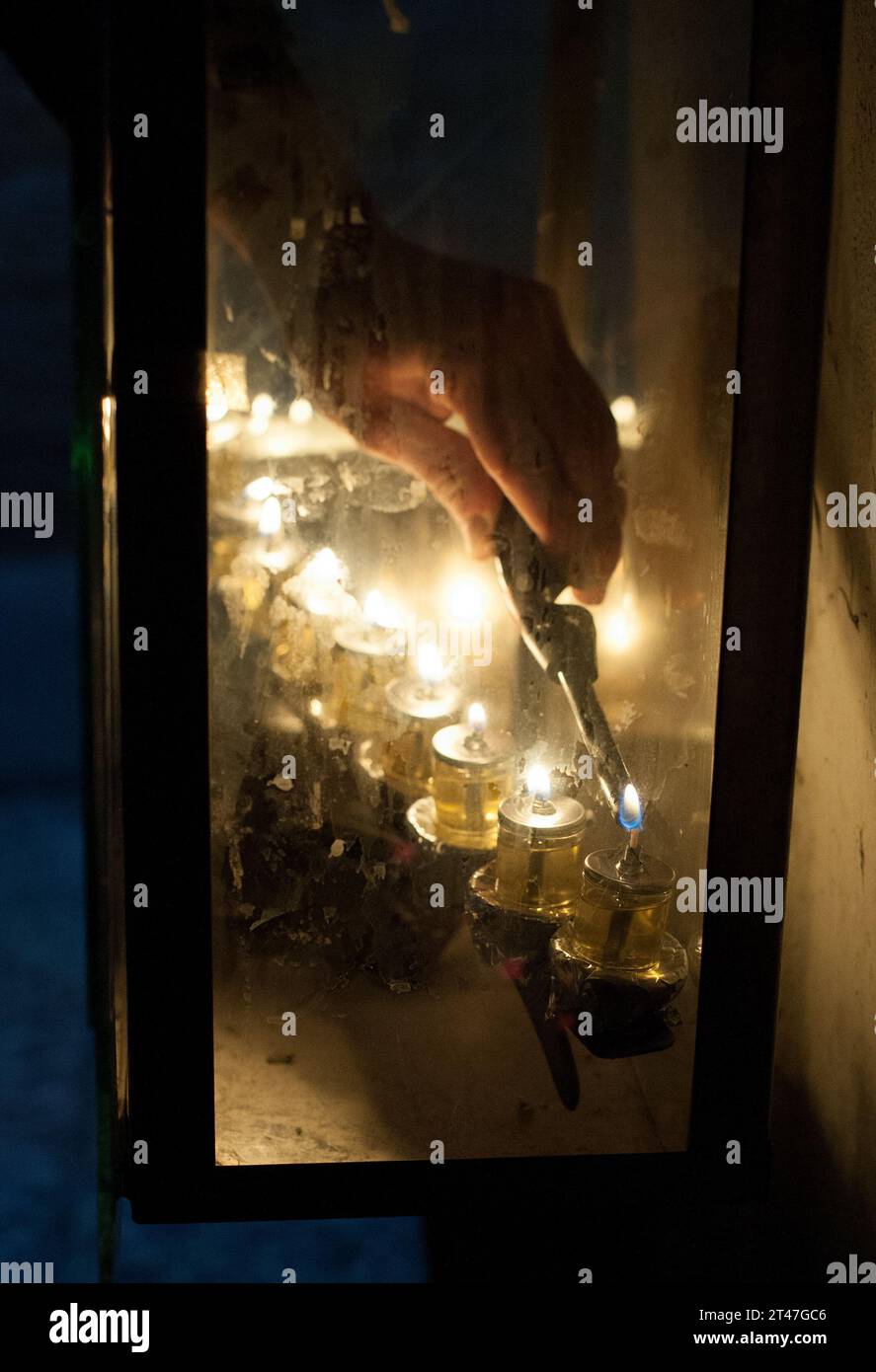 Closeup of a man's hand holding a candle and lighting the Hanukkah menorah oil lamps during the