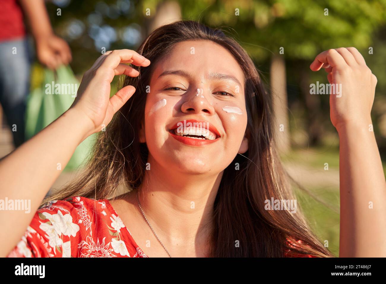 woman putting sunscreen on her face. smiling young latina with long