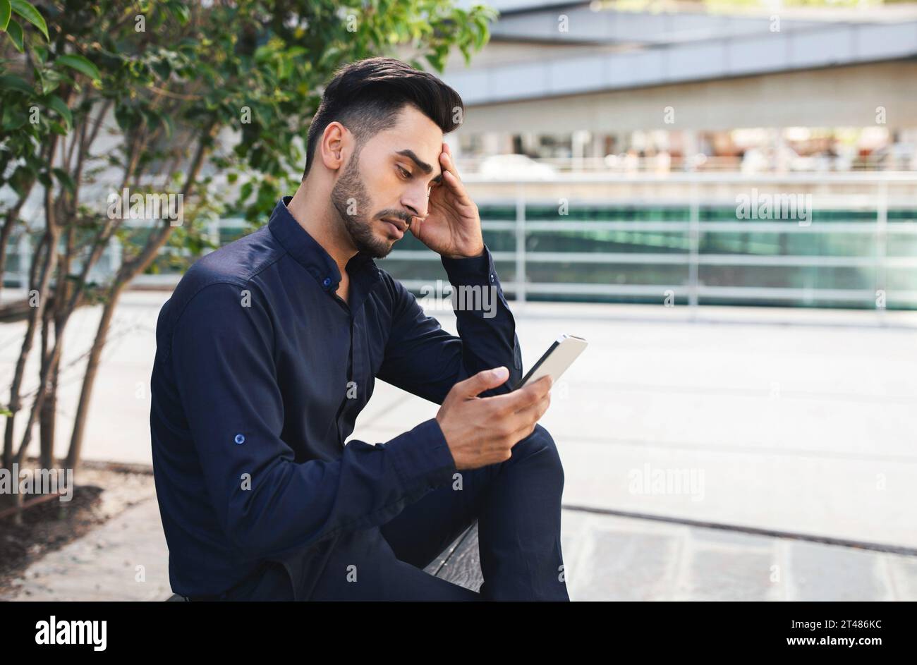 Stressed Middle Eastern business guy using app on phone outside Stock Photo