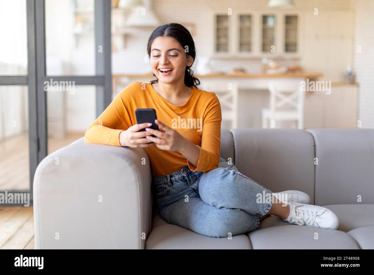 Smiling Young Indian Woman With Smartphone Relaxing On Couch At Home ...