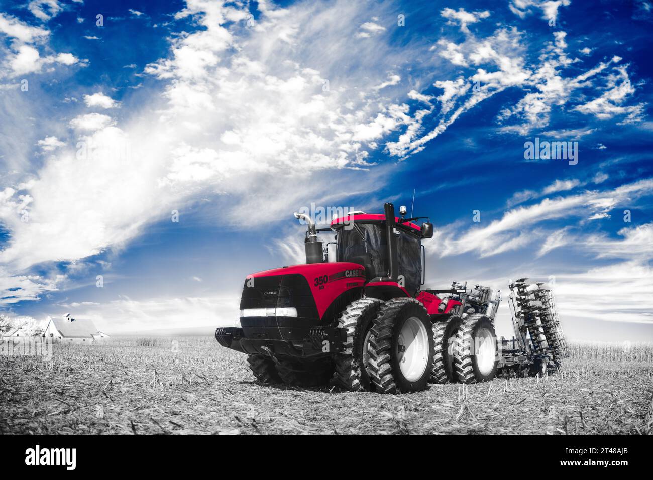 A red Case IH articulating tractor with a disc attached to it rests beneath a vibrant blue October sky in a field of corn stubble. Barn in distance. Stock Photo